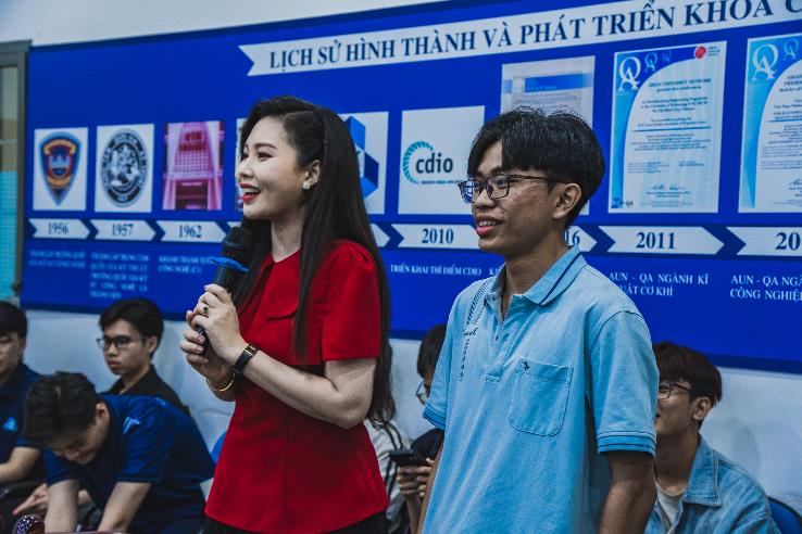 A person holding a microphone and a person standing in front of a blue board

AI-generated content may be incorrect.